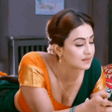 a woman in a saree is laying on her stomach on a bed looking at her phone .