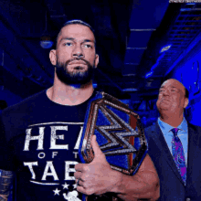 a man wearing a shirt that says he of sae holds a wrestling championship belt