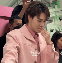 a man in a pink jacket and tie is covering his mouth with his hand and the words dec flower are visible