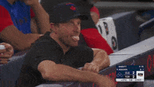 a man in a baseball cap sits in the dugout watching a baseball game
