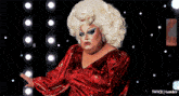 a drag queen is wearing a red dress and has a large blonde wig