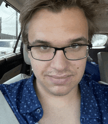 a man wearing glasses and a blue shirt is sitting in the back seat of a car