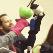 a man is holding a pink puppet and a green puppet in his hands