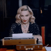 a woman is sitting at a desk with a typewriter and looking at the camera .