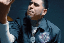 a man with a beard and tattoos is wearing a blue shirt and giving the middle finger .