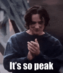 a man in a blue sweatshirt is clapping his hands with the words `` it 's so peak '' written on the bottom .