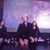 a group of women are dancing on stage in front of a large screen .