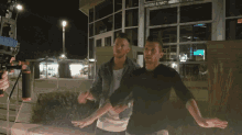 two men are standing in front of a building and one has a watch on his arm
