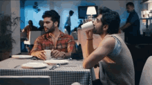 two men are sitting at a table in a restaurant drinking from cups