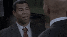 a man in a suit and tie is smiling while another man looks on