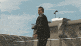 a man in a black leather jacket is standing on a rooftop holding a camera