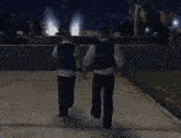two men are walking down a sidewalk holding hands at night