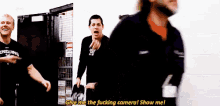 a group of men are standing in a room and one of them is saying " give me the fucking camera ! show me ! "