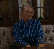a woman in a blue and white striped shirt is sitting at a table with a glass of orange juice