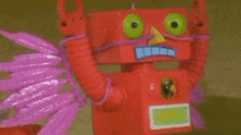 a red robot with green eyes and purple wings is standing in front of a green background