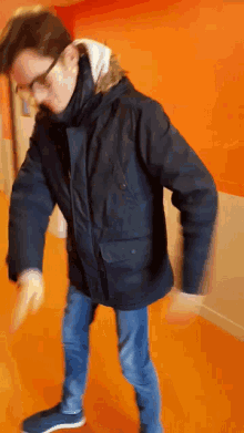 a man wearing glasses and a black jacket is standing in front of an orange wall