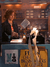 a woman standing behind a counter with a sign that says please check bags / bags at counter