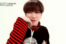 a young man in a red and black striped sweater is drinking from a plastic bottle .