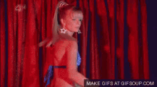 a woman in a blue and white bikini is dancing in front of a red curtain .