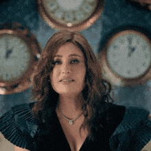a woman in a black dress is standing in front of a wall with clocks on it .