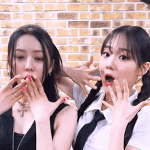 two girls are making funny faces with their hands over their mouths in front of a brick wall