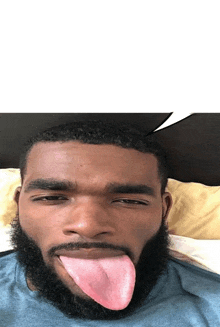 a man with a beard sticking his tongue out while laying on a bed