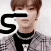 a man wearing a plaid jacket and a black turtleneck is holding a letter s in front of his face .