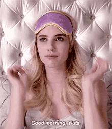 a woman wearing a purple sleep mask is laying on a bed and saying `` good morning , sluts . ''