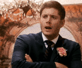 a man in a suit and tie is standing with his arms crossed and making a funny face .