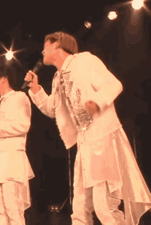 a man in a white jacket is singing into a microphone on stage