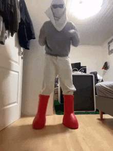 a person wearing a mask and red rain boots is dancing in a bedroom .