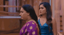 a woman in a purple sari is standing next to another woman in a red dress .