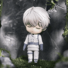 a figurine of a boy with white hair and blue gloves is standing in the grass .