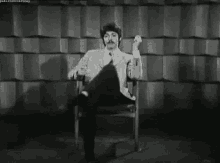 a man in a suit and tie is sitting in a chair and smoking a cigarette .
