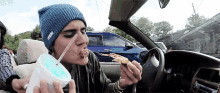a man in a blue beanie is eating a slice of pizza in a car .