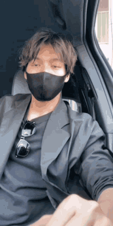 a man wearing a black mask and sunglasses sits in a car