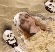 a woman is laying in the sand with skulls around her .