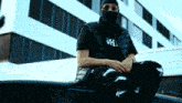 a man wearing a mask sits on top of a black car