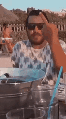 a man wearing sunglasses is giving the middle finger while sitting at a table