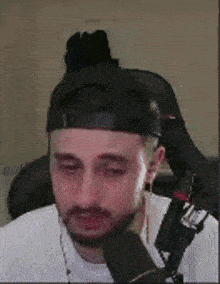 a man with a beard is sitting in front of a microphone wearing a baseball cap .