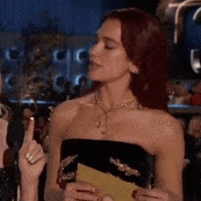 a woman with red hair is wearing a black strapless dress and a gold necklace while talking into a microphone .