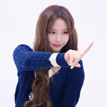 a woman in a blue sweater is pointing her finger at the camera