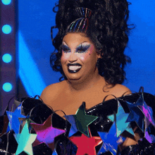 a drag queen wearing a black top with stars on it smiles