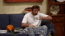 a man is sitting on a couch drinking a cup of coffee with a foreign language written on it