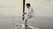 a man in a white suit is sitting on the side of a boat in the ocean