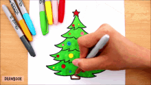 a person is drawing a christmas tree with sharpie markers in the background