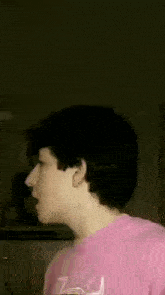 a young man wearing a pink t-shirt is looking at the camera .
