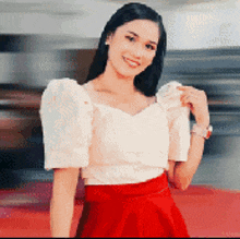 a woman wearing a white top and a red skirt is smiling