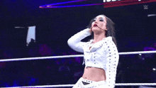a woman in a white jacket is giving the ok sign while standing in a wrestling ring .