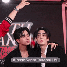 two young men are posing for a photo with a sign that says #perthsantafanconlive